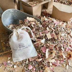 May include: A small white muslin bag with the text "Fruit and Flower Shop" printed on it. The bag is filled with a mixture of dried lavender, wood shavings, and pink flower petals. The bag is sitting on a pile of the same mixture.
