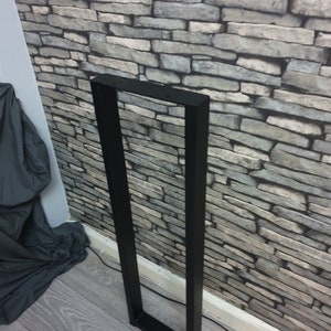 May include: Black metal table leg with a rectangular frame. The leg is standing on a wood floor.