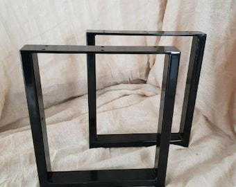 May include: Two black metal table legs with a square design. The legs are made of sturdy metal and have a black finish.