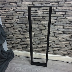 May include: Black metal table legs with a rectangular shape. The legs are standing on a wooden floor.