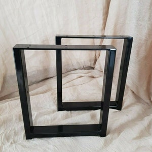 May include: Two black metal table legs with a square shape and a flat base. The legs are made of sturdy metal and have a black powder coat finish.
