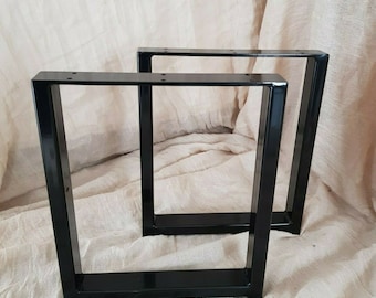 May include: Two black metal table legs with a square shape and a flat base. The legs are made of sturdy metal and have a black powder coat finish.
