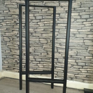 May include: Two black metal table legs, one taller than the other, standing on a wooden floor. The legs are made of square tubing and have a simple, modern design.