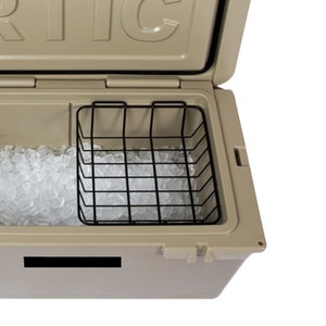 May include: Tan cooler with an open lid, revealing a black wire basket and ice. The cooler has a rectangular shape and a handle on the side. The interior is filled with ice cubes, and the basket is positioned to hold items.