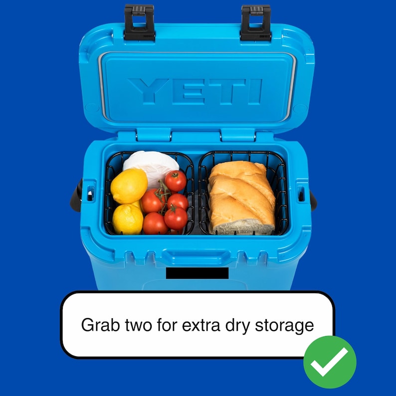 Puede incluir: Nevera azul abierta con la marca "YETI" visible en la tapa. En el interior, dos cestas de alambre negro contienen alimentos: limones, tomates, pan y un art&iacute;culo blanco. El texto "Grab two for extra dry storage" se muestra debajo.