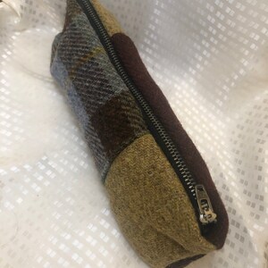 May include: A brown, green and blue patchwork zipped pouch. The pouch is made of a soft, textured fabric.