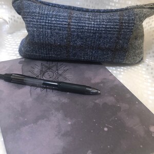 May include: A blue and grey plaid zippered pouch with a black pen and a grey notebook with the word "CREATIVITY" printed on it.