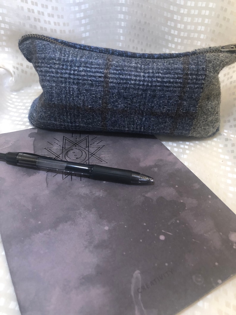 May include: A blue and grey plaid zippered pouch with a black pen and a grey notebook with the word "CREATIVITY" printed on it.