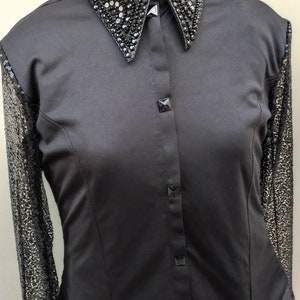 Puede incluir: Una camisa negra de botones con un cuello grande adornado. El cuello est&aacute; decorado con diamantes de imitaci&oacute;n y lentejuelas negras. La camisa tiene mangas largas con una superposici&oacute;n de encaje negro.
