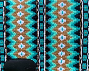 May include: A turquoise, brown, and white woven saddle pad with a black border. The saddle pad has a geometric pattern and a black leather girth strap.