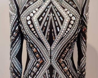 May include: A black show jacket with a silver and white geometric design. The jacket is embellished with rhinestones and beads. The text "Alina by Alina" is printed on the bottom of the jacket.