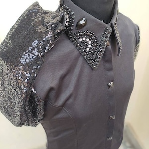 Puede incluir: Una camisa negra de manga corta con un hombro de lentejuelas y un cuello negro adornado.