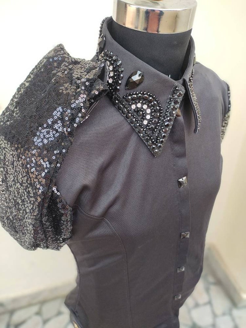 Puede incluir: Una camisa negra de manga corta con un hombro de lentejuelas y un cuello negro adornado.