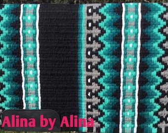 May include: A black, teal, gray, and white woven horse saddle pad with a geometric pattern. The saddle pad has the text "Alina by Alina" on the bottom.