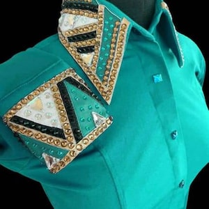May include: Teal long-sleeve shirt with a gold, black, and green geometric design on the collar and one sleeve. The design features rhinestones and a white fabric accent.