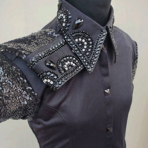 Puede incluir: Una camisa negra de botones con un cuello grande adornado. El cuello est&aacute; cubierto de lentejuelas y pedrer&iacute;a negras.