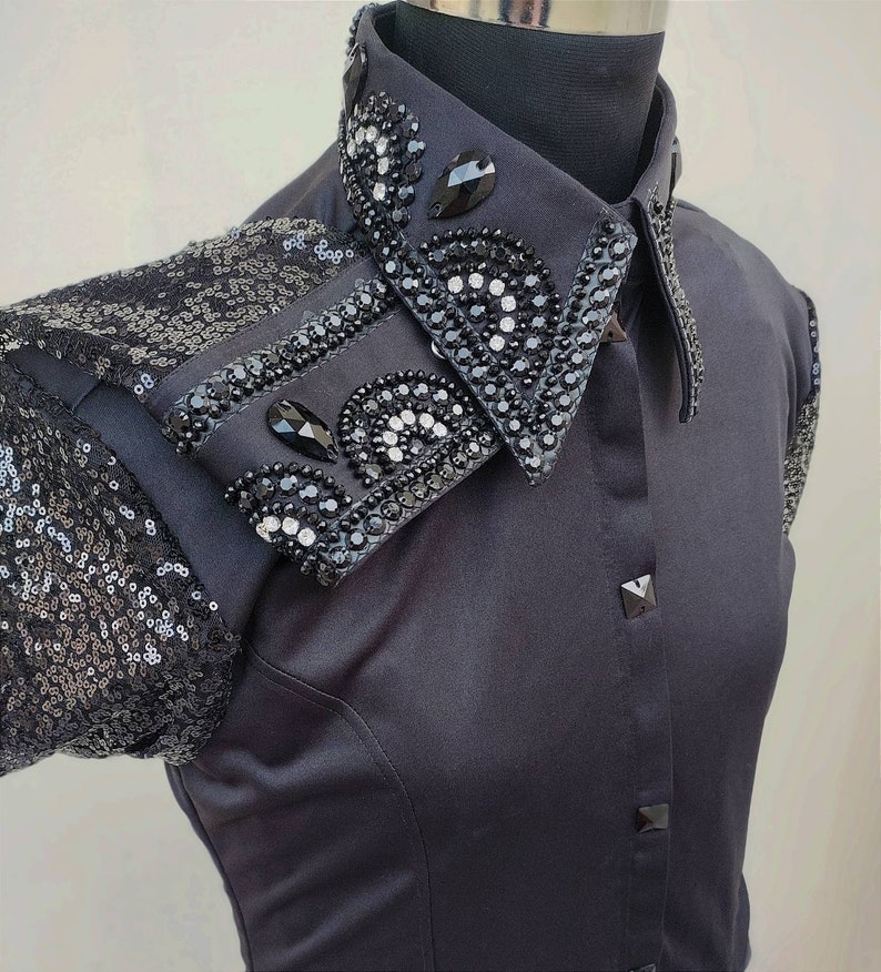 Puede incluir: Una camisa negra de botones con un cuello grande adornado. El cuello est&aacute; cubierto de lentejuelas y pedrer&iacute;a negras.