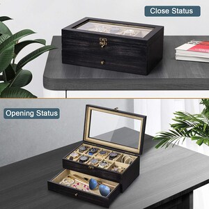 May include: A black wooden watch box with a glass top and a drawer. The box is open and has multiple watch compartments. The drawer is open and contains sunglasses, a necklace, and a pen.