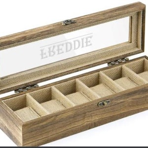 May include: A wooden watch box with a glass top and six compartments lined with brown fabric. The box is engraved with the name "LKEDDIE".