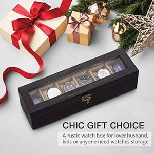 May include: A black wooden watch box with a glass top and six compartments for storing watches. The box has a gold latch and is sitting on a white surface.