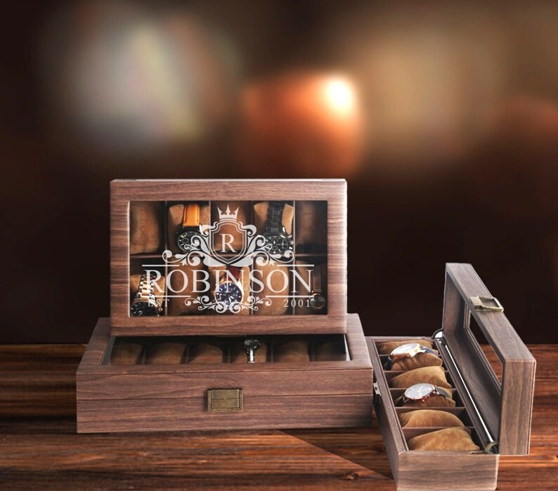 May include: A wooden watch box with a glass top and a personalized inscription that reads "R ROBINSON 2001". The box has a brown finish and is open to reveal a velvet interior with slots for watches.