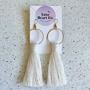 May include: White tassel earrings with gold hoops. The earrings are displayed on a white card with the text "Luxe Heart Co. Macrame & Accessories".