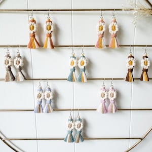 May include: A display of handmade crocheted flower earrings with various colour combinations, including blue, pink, yellow, and brown. The earrings are displayed on a gold metal rack.