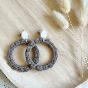 May include: A pair of brown crocheted hoop earrings with white round accents. The earrings are displayed on a wooden tray.