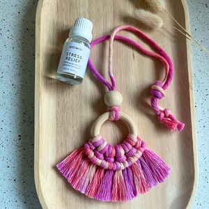 May include: A pink and white macrame tassel necklace with a wooden ring and a small bottle of essential oil labelled "Stress Relief".