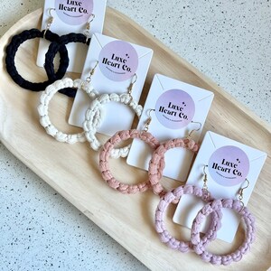 May include: Four pairs of handmade macrame hoop earrings displayed on white cards with the logo "Luxe Heart Co." The earrings are in black, white, light pink, and a darker shade of pink.