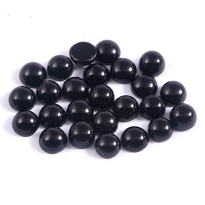 May include: A collection of glossy, black cabochon gemstones, each with a smooth, rounded surface. The gemstones are scattered across a white background, showcasing their polished appearance. These stones are ideal for jewelry making.