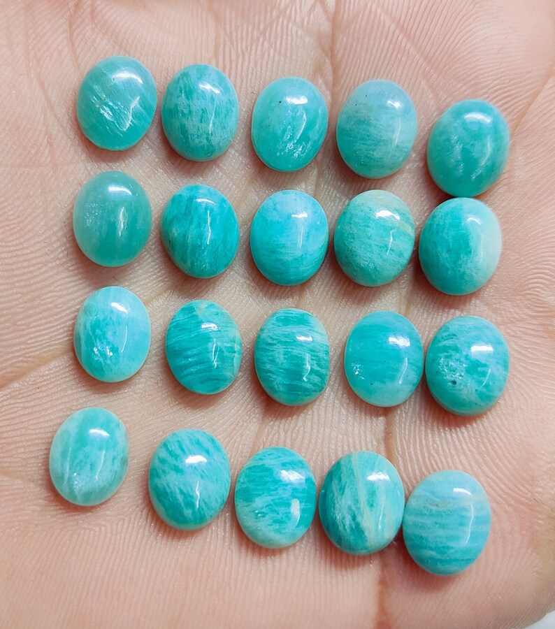 Pu&ograve; includere: Una collezione di gemme di Amazonite ovali in varie tonalit&agrave; di verde acqua e turchese. Le pietre lucide mostrano motivi naturali e sono disposte su una superficie chiara, evidenziando la loro finitura liscia e lucida. Ideali per la creazione di gioielli.