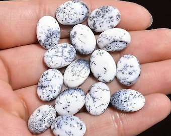 Op de afbeelding: Een verzameling ovale, witte edelstenen met ingewikkelde zwarte patronen. De gepolijste stenen hebben een gespikkelde en geaderde uitstraling. De edelstenen worden in een hand gehouden, waarbij hun grootte en details worden getoond. Ideaal voor het maken van sieraden.