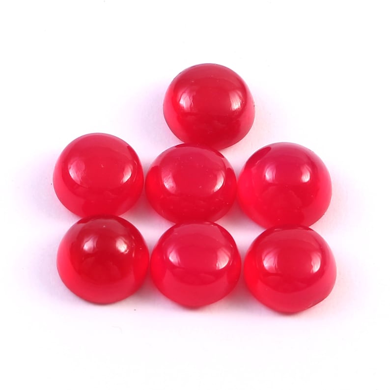 Peut inclure: Sept cabochons rouges brillants sur fond blanc. Les cabochons sont ronds avec une surface lisse et polie. Les pierres pr&eacute;cieuses sont d'un rouge vif et uni.