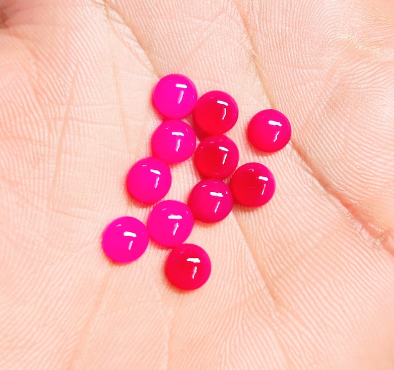 Peut inclure: Un ensemble de petites perles rondes et brillantes dans des tons de rose et de rouge. Les perles sont dispers&eacute;es sur une surface claire, cr&eacute;ant un affichage vibrant et accrocheur. Ces perles peuvent &ecirc;tre utilis&eacute;es pour la fabrication de bijoux ou d'autres projets d'artisanat.