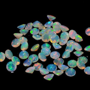 May include: A collection of opals with a black background. The opals are a mix of shapes, including oval, round, and triangular. They display a play of color with flashes of blue, green, and orange. The gemstones are scattered across the surface.