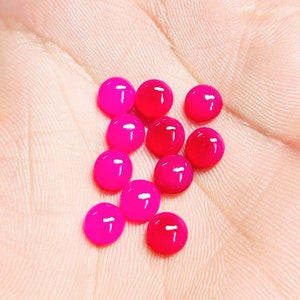 Peut inclure: Une collection de petites perles rondes et brillantes dans des tons de rose et de rouge. Les perles sont dispers&eacute;es sur une surface claire, avec quelques perles d'une teinte rouge plus fonc&eacute;e. Les perles ont un aspect lisse et poli.
