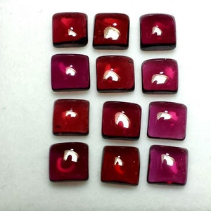 Puede incluir: Doce gemas cuadradas pulidas en tonos rojos y magenta. Las gemas están dispuestas en una cuadrícula, cada una con esquinas redondeadas y una superficie reflectante. Adecuado para la creación de joyas.