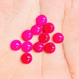 Peut inclure: Un ensemble de cabochons ronds, brillants et roses vifs. Les cabochons sont dispos&eacute;s sur une surface rose clair, mettant en valeur leur aspect lisse et poli. Ces petites gemmes color&eacute;es sont id&eacute;ales pour la cr&eacute;ation de bijoux ou les projets d'artisanat.