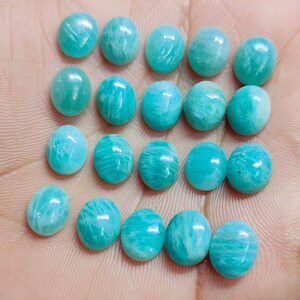 Pu&ograve; includere: Una collezione di pietre preziose di Amazonite di forma ovale, ognuna con una vibrante tonalit&agrave; turchese con sottili venature naturali. Le pietre lucide sono disposte vicine, mostrando le loro superfici lisce e lucenti. Ideali per la creazione di gioielli.