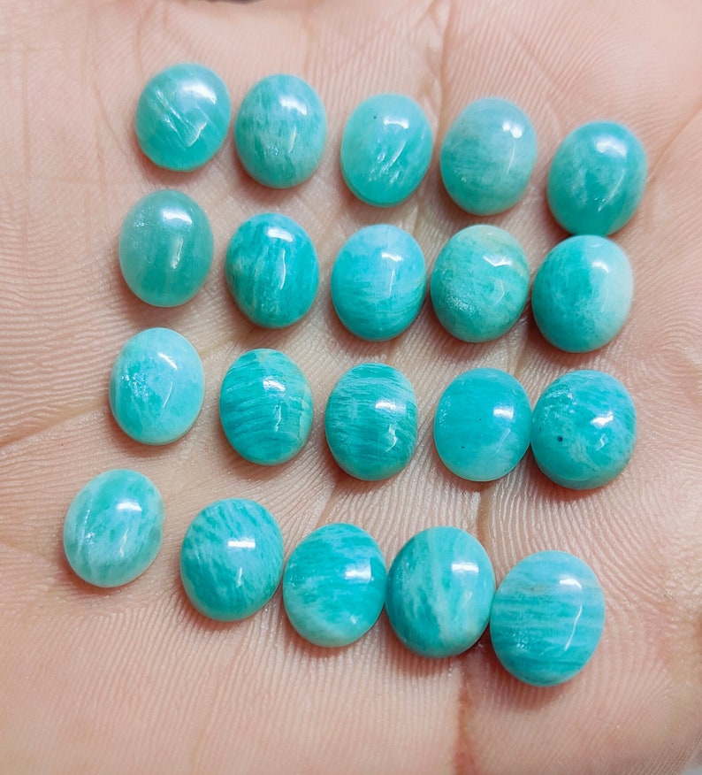 Pu&ograve; includere: Una collezione di pietre preziose di Amazonite di forma ovale, ognuna con una vibrante tonalit&agrave; turchese con sottili venature naturali. Le pietre lucide sono disposte vicine, mostrando le loro superfici lisce e lucenti. Ideali per la creazione di gioielli.