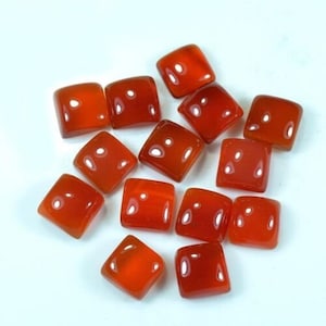 May include: A collection of square, polished carnelian gemstones. Each stone is a vibrant orange-red color with rounded corners and a glossy finish. The gemstones are scattered on a white surface.