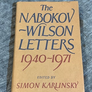 May include: A hardcover book with a tan dust jacket featuring dark blue and maroon text. The title reads The NABOKOV-WILSON LETTERS 1940-1971, EDITED BY SIMON KARLINSKY. The cover has a subtle vertical lined texture throughout the tan background.