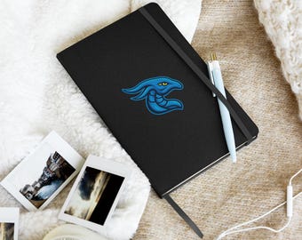 May include: Black notebook with a blue and teal logo of a stylized creature. A light blue pen rests on the notebook, along with several small photographs and a white camera. White earbuds are also visible.