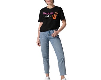 May include: A black t-shirt with the text "KELKÜÄ HAPXİ" in pink and orange, along with a handprint graphic. The person is wearing light blue jeans and white sneakers.