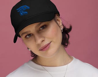 May include: Black baseball cap featuring a blue embroidered dragon design on the front. The cap has a curved brim and a structured fit. The dragon has yellow eyes and is set against a black background. The cap is worn by a person.
