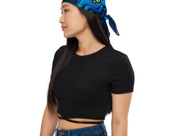 May include: A dark blue bandana featuring a cartoon octopus design with yellow eyes and blue tentacles. The bandana is tied at the back. The person is wearing a black crop top and blue jeans.