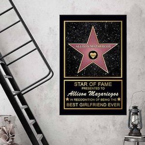 Op de afbeelding: Een zwarte en gouden gegraveerde plaquette met een roze ster en de tekst "Allison Mazariegos" en "STAR OF FAME PRESENTED TO Allison Mazariegos IN RECOGNITION OF BEING THE BEST GIRLFRIEND EVER".