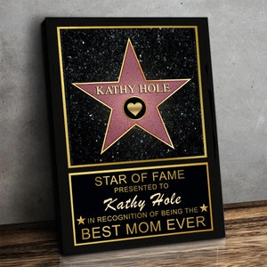 Op de afbeelding: Een zwarte en gouden gegraveerde plaquette met een roze ster en de tekst "Kathy Hole" in gouden letters. De plaquette luidt "Star of Fame Presented to Kathy Hole In recognition of being the Best Mom Ever".
