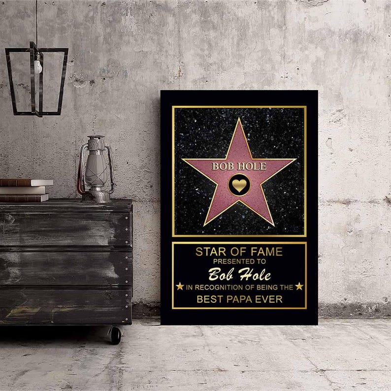 Op de afbeelding: Een zwart en gouden ingelijst afdruk met een roze ster op een zwarte achtergrond. De ster heeft de tekst "BOB HOLE" en een hart in het midden. De tekst onder de ster luidt "STAR OF FAME PRESENTED TO Bob Hole IN RECOGNITION OF BEING THE BEST PAPA EVER".